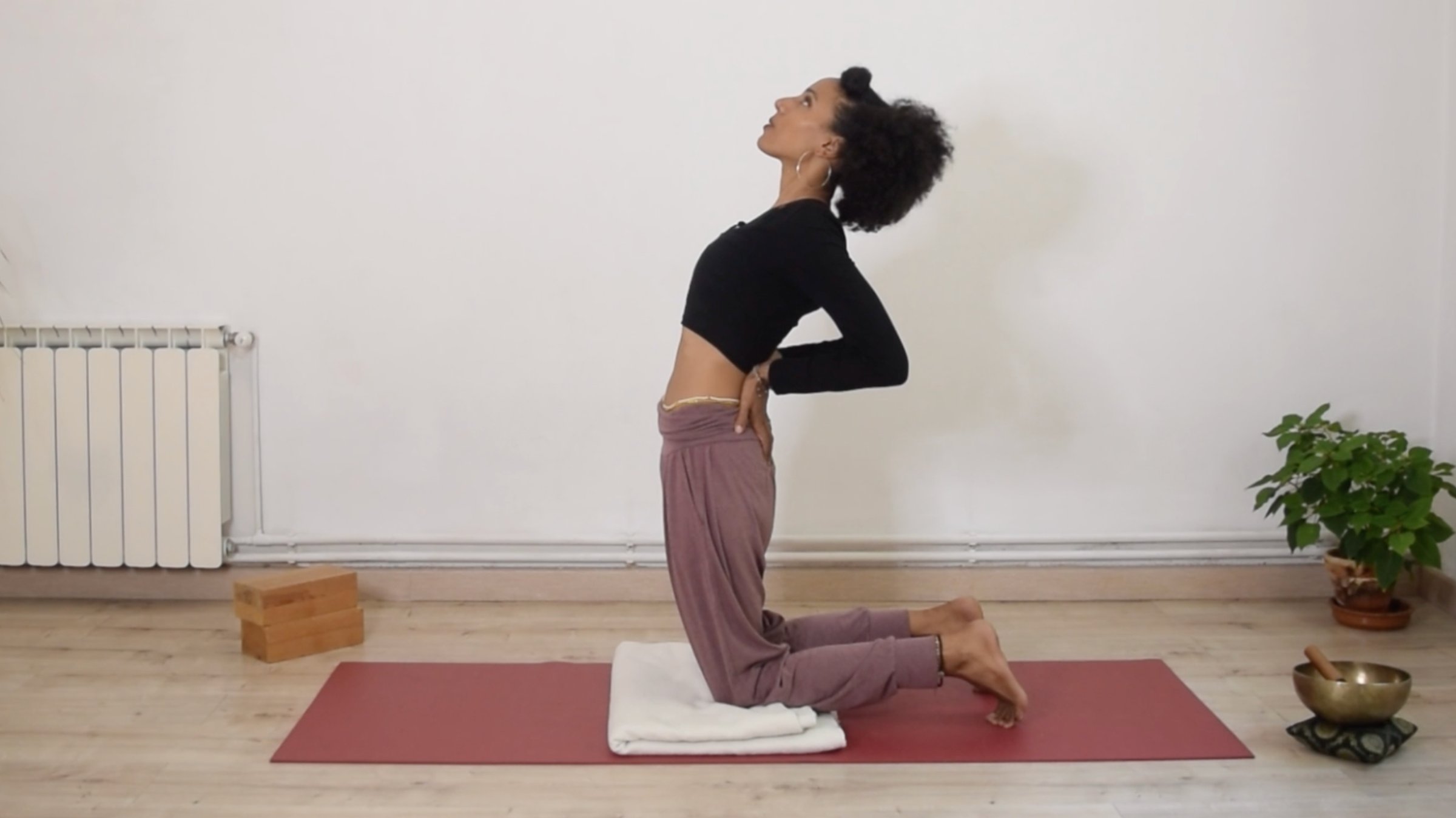 Yoga instructor Laia Bové kneeling on a yoga mat in a supported Camel Pose with her hands on her hips.